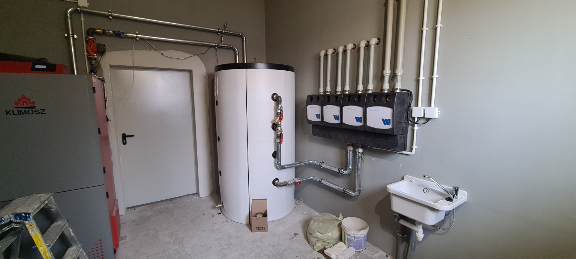 Installation of four Watts FlowBox DN25 pump groups with a boiler manifold, connected to a pellet boiler and a 1,000-liter heat storage tank for a 2,000 m² hall